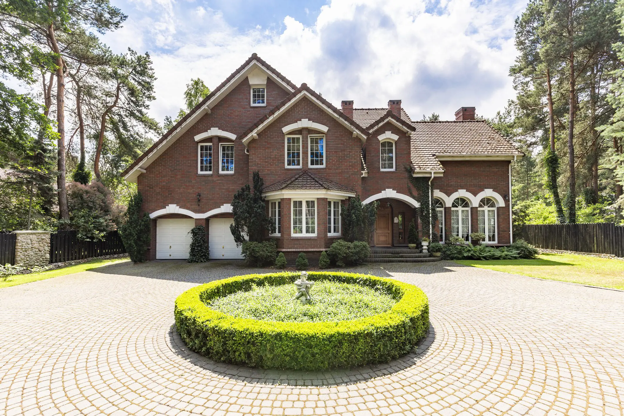 Front view of a driveway with a round garden and big, english style house in the background. Real photo